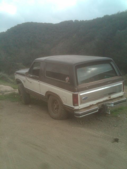 1982 Ford Bronco - Rear view of a two-tone 1980 Ford Bronco on a dirt road with hills in the background.