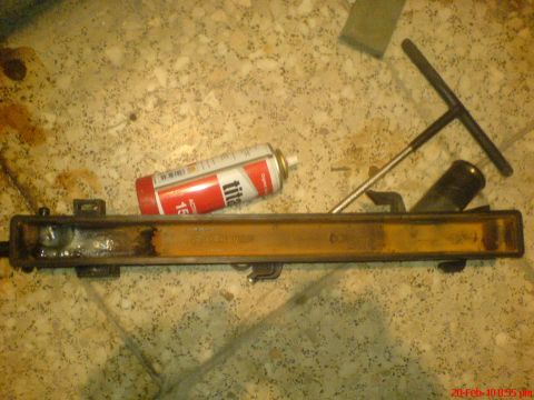1998 Ford Crown Victoria - A radiator part, spray can, and T-handle tool are laid out on a speckled floor, likely for repair work.