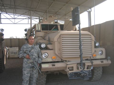 1995 Ford Bronco - A soldier stands before a large tan military truck, which appears to be parked under a covered structure.