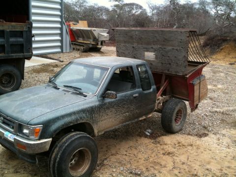 1993 Ford Bronco - A dark green pickup truck with a custom wooden box in the bed is parked on a dirt lot next to other vehicles and equipment.