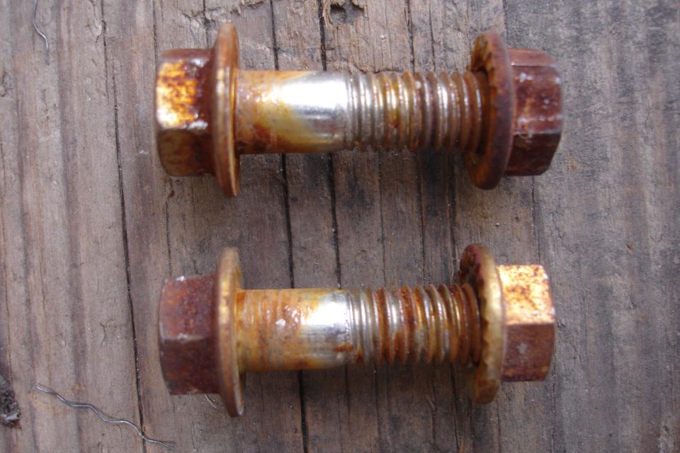 two rusty bolts with integrated washers on a wooden surface