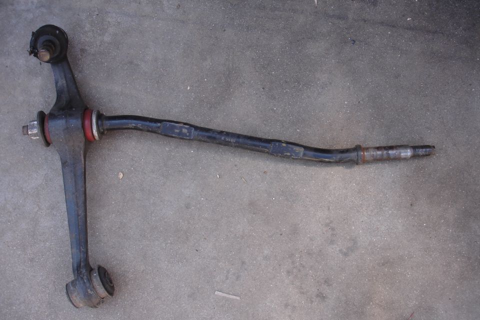 Automotive suspension control arm with red and black bushings, lying on concrete