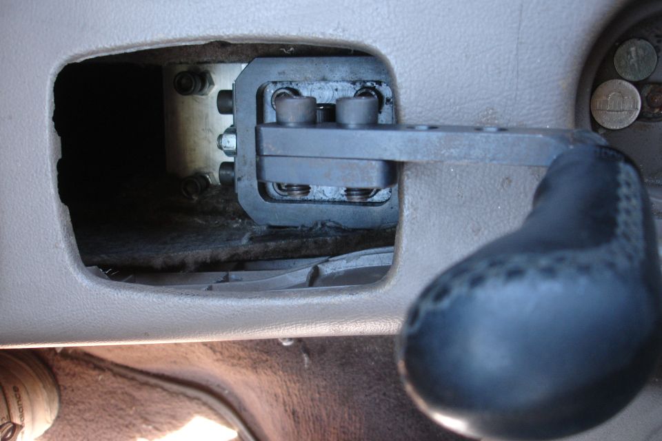 Close-up of a car's interior showing a metal short shifter mechanism installed in the center console, with coins visible in a nearby compartment