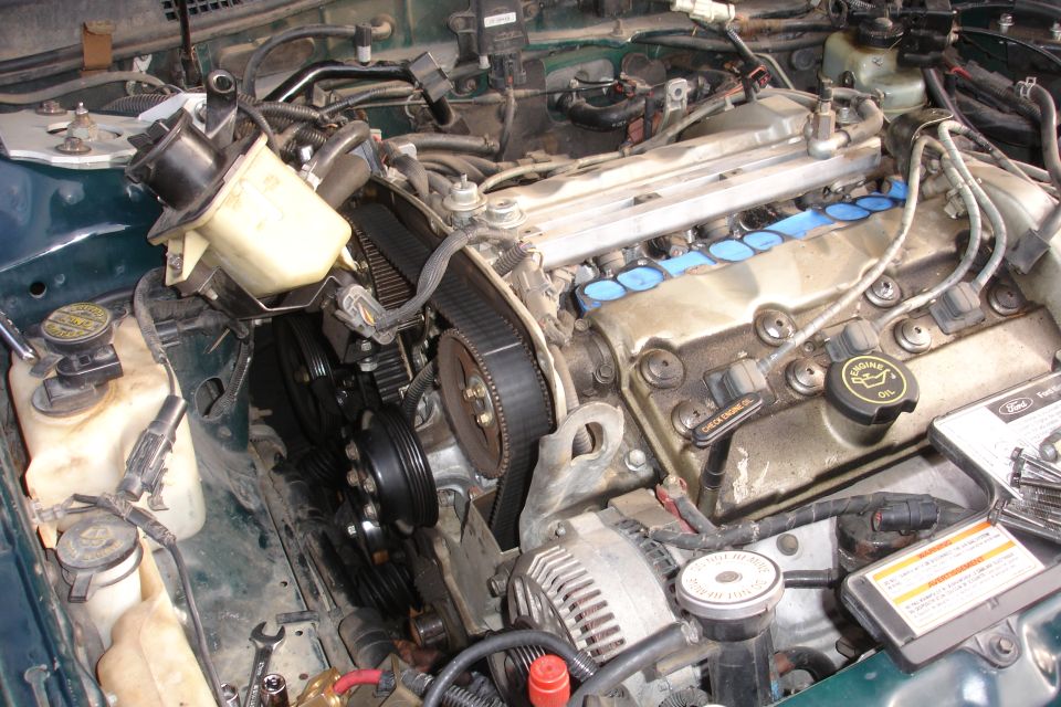Engine bay with timing belt exposed, power steering reservoir, and alternator. Green exterior paint visible