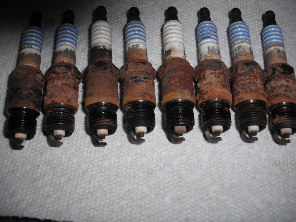 eight rusty spark plugs on a white cloth