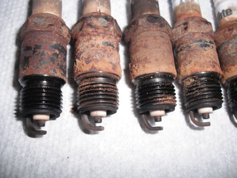 1991 Ford Bronco - Close-up view of four used and corroded spark plugs, likely needing replacement.