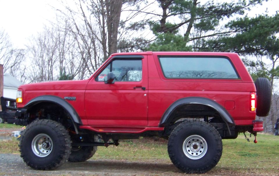 Lifted red Ford Bronco SUV with black fender flares and big tires, side view on grass