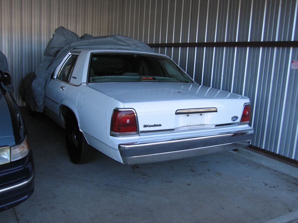 1991 Ford Crown Victoria LTD parked in storage unit, partially covered by a tarp. Another vehicle is visible to the left