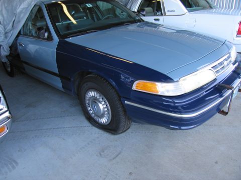 1991 Ford LTD Crown Victoria - A two-tone Ford Crown Victoria with a flat tire sits in a garage next to another vehicle.