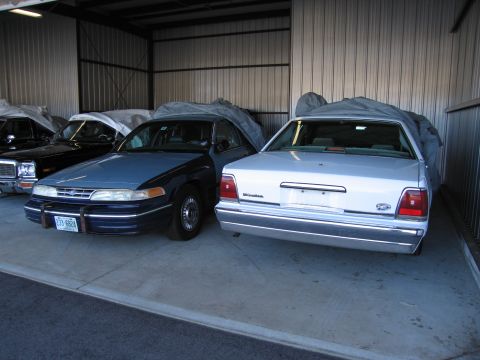 1991 Ford LTD Crown Victoria - Two sedans, a blue 1991 Ford Crown Victoria LTD and a white sedan, are parked inside a garage.