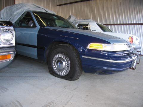1991 Ford LTD Crown Victoria - A two-tone Ford Crown Victoria with a flat tire sits in a garage next to another vehicle.