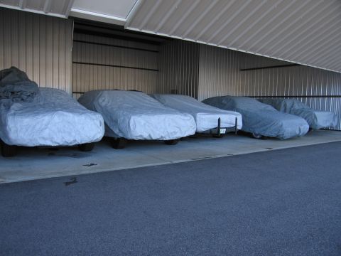 1991 Ford LTD Crown Victoria - Multiple vehicles are stored under protective covers within a large, open-air garage structure.