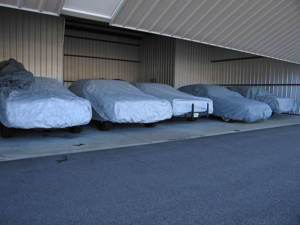 Several cars covered in tarps parked inside a metal building
