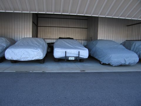 1991 Ford LTD Crown Victoria - Multiple vehicles are stored under car covers inside a metal garage structure.