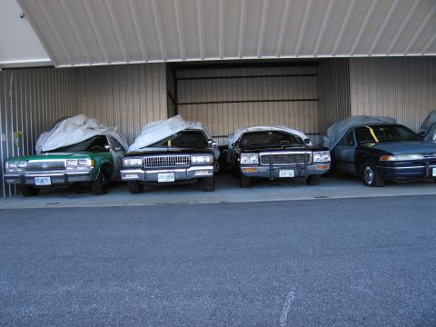 1991 Ford LTD Crown Victoria - Several vehicles are stored under covers inside a metal-sided garage.