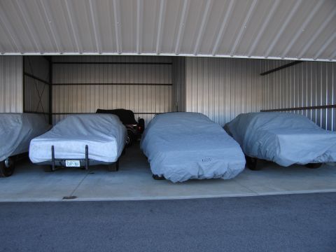 1991 Ford LTD Crown Victoria - Multiple vehicles are stored under protective covers inside a metal structure.