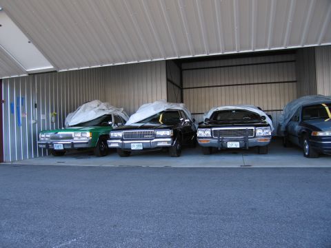 1991 Ford LTD Crown Victoria - Several vehicles are stored under cover in a metal storage unit.