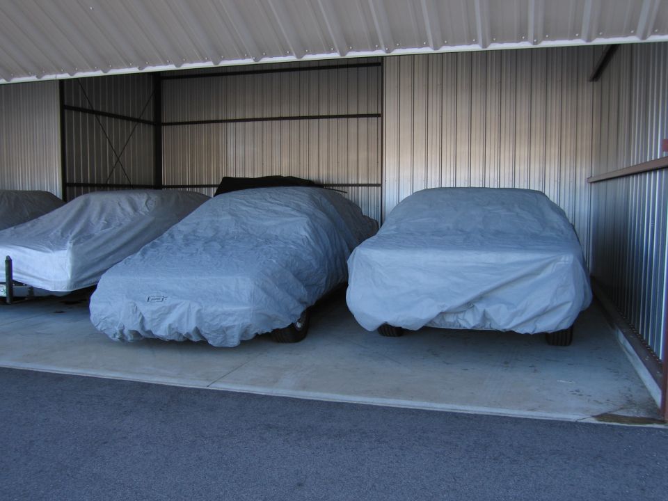 Three cars covered with gray tarps parked inside a metal storage unit