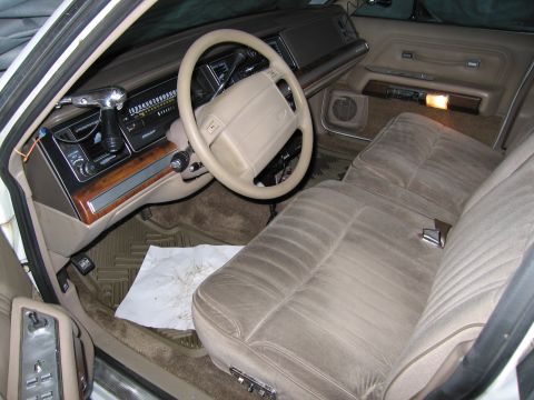 1991 Ford LTD Crown Victoria - The interior of a car shows tan velour seats, a tan steering wheel, and wood trim accents on the dashboard and door panels.