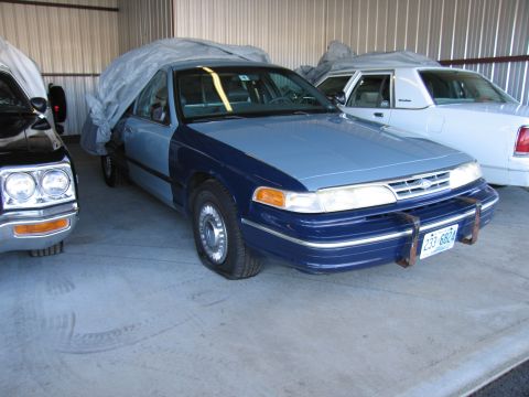 1991 Ford LTD Crown Victoria - A 1991 Ford Crown Victoria LTD, partially covered, sits with a flat tire next to another vehicle in a garage.