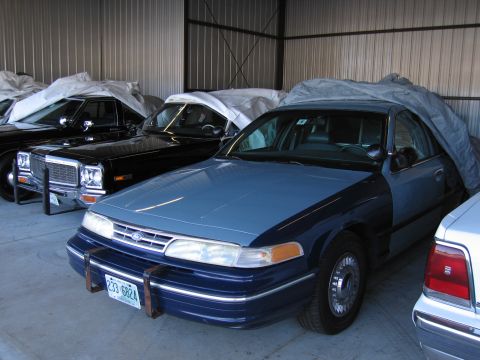 1991 Ford LTD Crown Victoria - A two-tone Ford Crown Victoria is covered by a tarp in a garage alongside other vehicles.