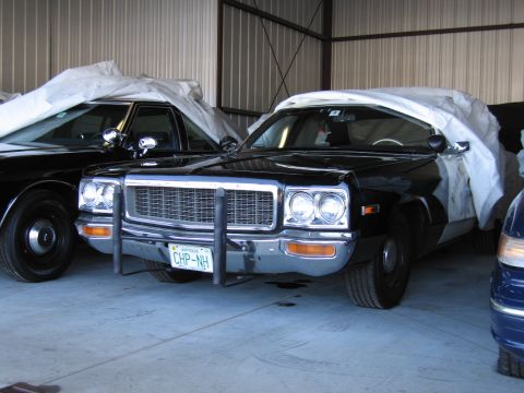1991 Ford LTD Crown Victoria - Two police cars are parked inside a garage, one partially covered.