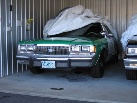 1991 Ford LTD Crown Victoria - A green and white 1991 Ford Crown Victoria LTD is parked in a garage, partially covered by a tarp, with another vehicle visible to the righ…