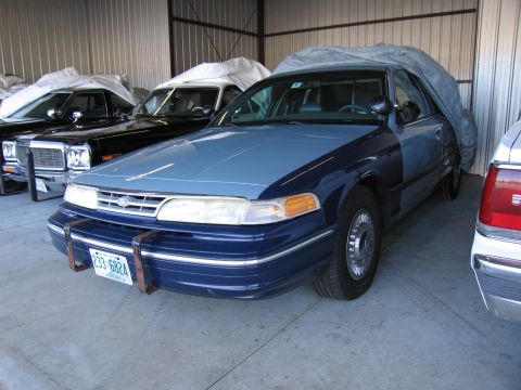 1991 Ford LTD Crown Victoria - A 1991 Ford Crown Victoria LTD police car, possibly a former patrol vehicle, is parked indoors with a tarp partially covering it.
