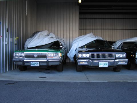 1991 Ford LTD Crown Victoria - Two cars are parked inside a garage, both covered with protective tarps.