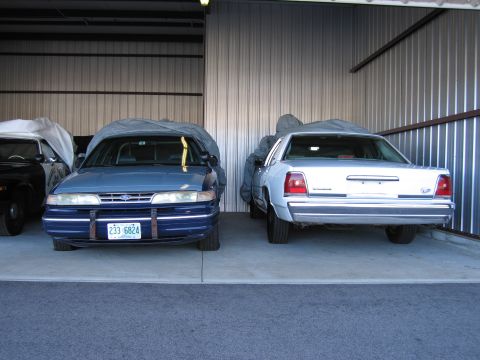 1991 Ford LTD Crown Victoria - Two sedans, including a blue 1991 Ford Crown Victoria LTD, are parked in a garage.