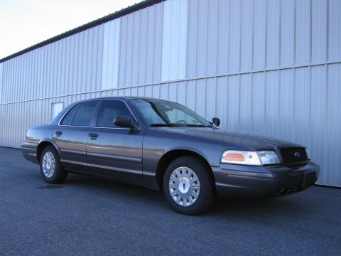 1991 Ford LTD Crown Victoria - A dark gray Ford Crown Victoria is parked in front of a large corrugated metal building.