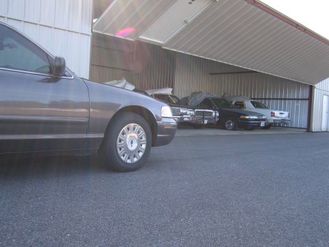 1991 Ford LTD Crown Victoria - A 1991 Ford Crown Victoria LTD is seen in a hangar alongside other vehicles, with its front quarter visible.