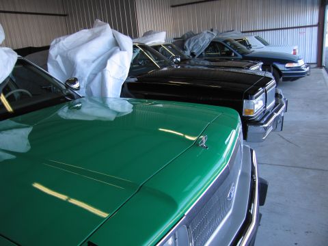 1991 Ford LTD Crown Victoria - A line of vehicles, including a green 1991 Ford Crown Victoria LTD, are stored indoors under protective coverings.