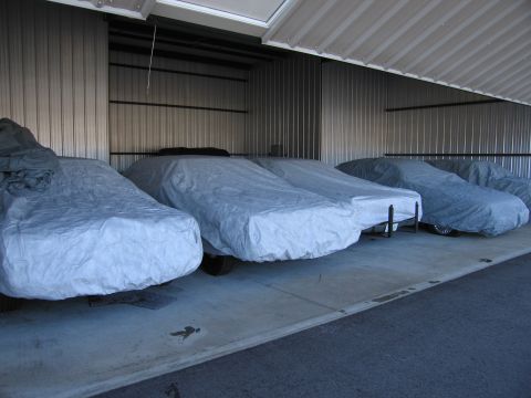 1991 Ford LTD Crown Victoria - Multiple vehicles are covered and stored in a row within a metal-sided storage unit.