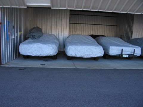 1991 Ford LTD Crown Victoria - Multiple vehicles are stored under covers in a corrugated metal garage.