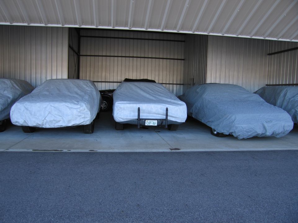 Three cars covered in gray car covers parked in a garage