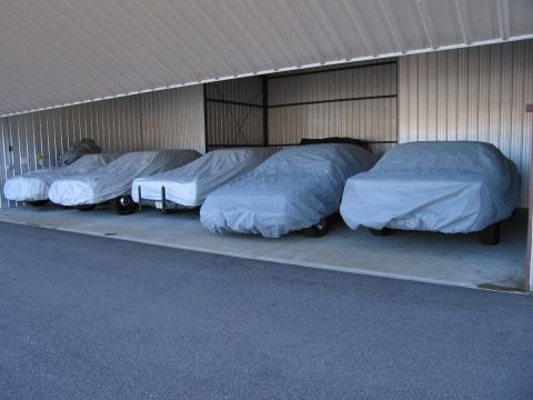 1991 Ford LTD Crown Victoria - Several vehicles are covered and stored indoors within a metal building.