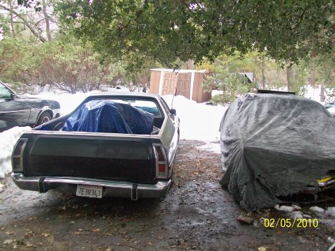 1973 Ford Ranchero - A 1973 Ford Ranchero is parked next to another vehicle covered by a tarp, with snow on the ground.