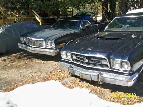1973 Ford Ranchero - Two Ford Rancheros are parked outside, one with a hood scoop and the other partially covered.
