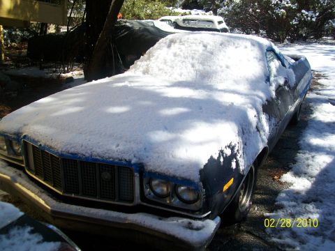 1973 Ford Ranchero - A dark blue Ford Ranchero sits covered in snow, with another vehicle partially visible behind it.