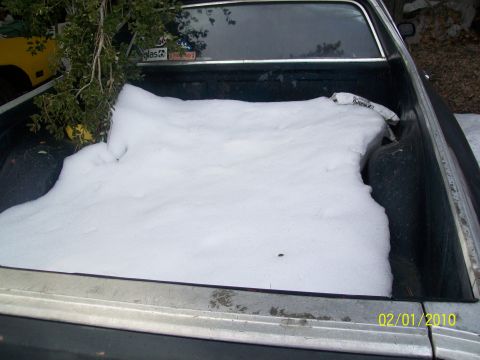 1973 Ford Ranchero - Snow covers the bed of a silver pickup truck, with a yellow vehicle partially visible behind it.