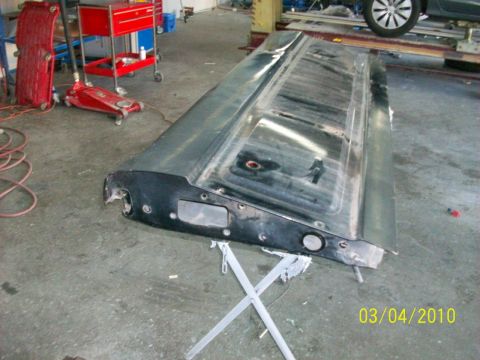 1985 Ford Bronco - A detached car tailgate panel is shown in a workshop setting, possibly undergoing repair or restoration.