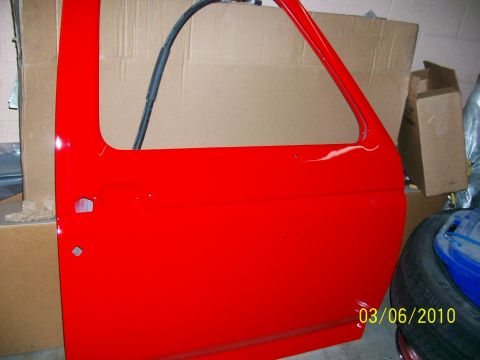 1985 Ford Bronco - A red vehicle door is shown with a black hose attached to the frame, set against a backdrop of cardboard boxes.