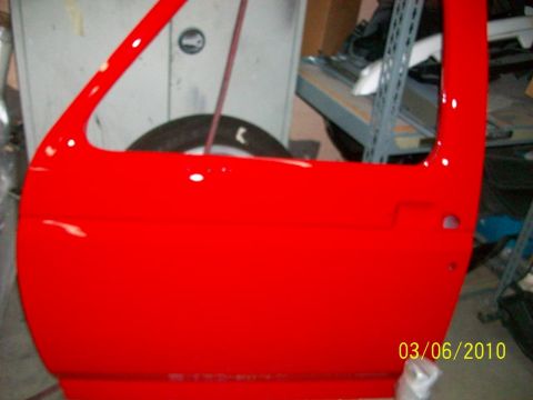 1985 Ford Bronco - A bright red car door is shown in a workshop, with a tire visible in the background.