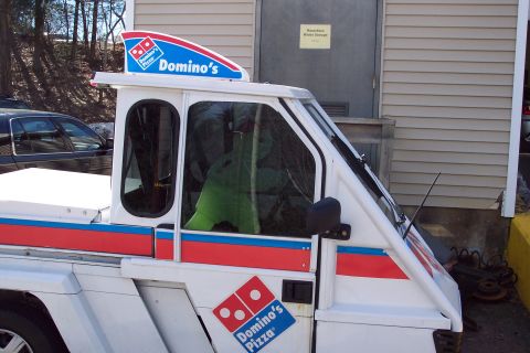 2001 Ford Crown Victoria - A Domino's Pizza branded delivery vehicle is parked outside a building with a hazardous waste storage sign.