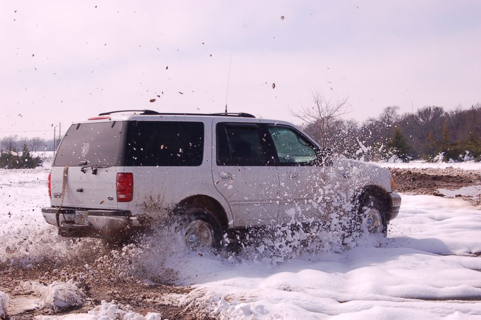2002 Ford Expedition driving through snow and mud, kicking up spray