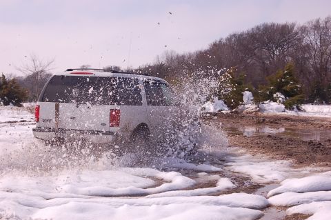 2002 Ford Expedition - A white 2002 Ford Expedition navigates a snowy and muddy terrain, creating a large spray.