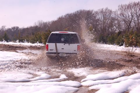 2002 Ford Expedition - A white 2002 Ford Expedition navigates a challenging muddy and snowy terrain, creating a large splash.
