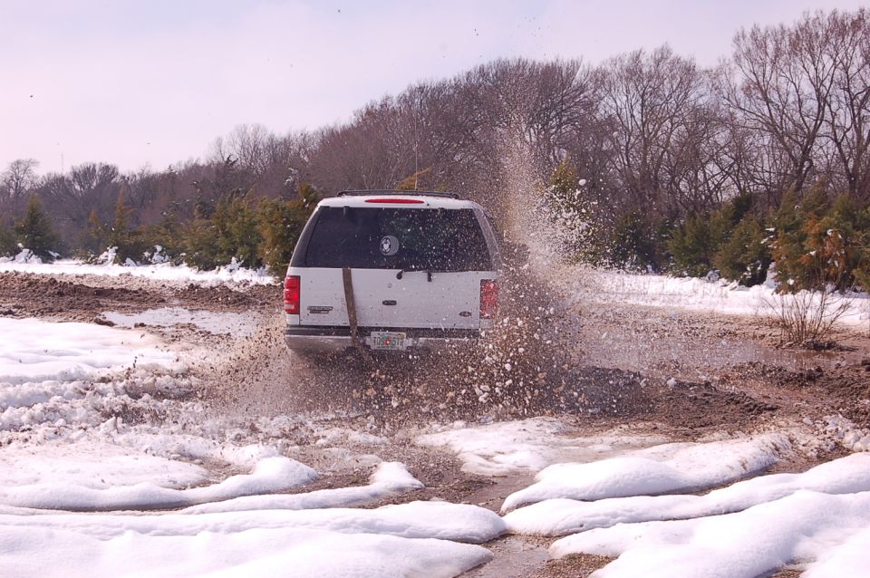 White 2002 Ford Expedition driving through a muddy, snowy area, kicking up water and dirt