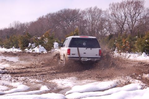 2002 Ford Expedition - A white 2002 Ford Expedition navigates a muddy and snowy terrain, kicking up a large spray.